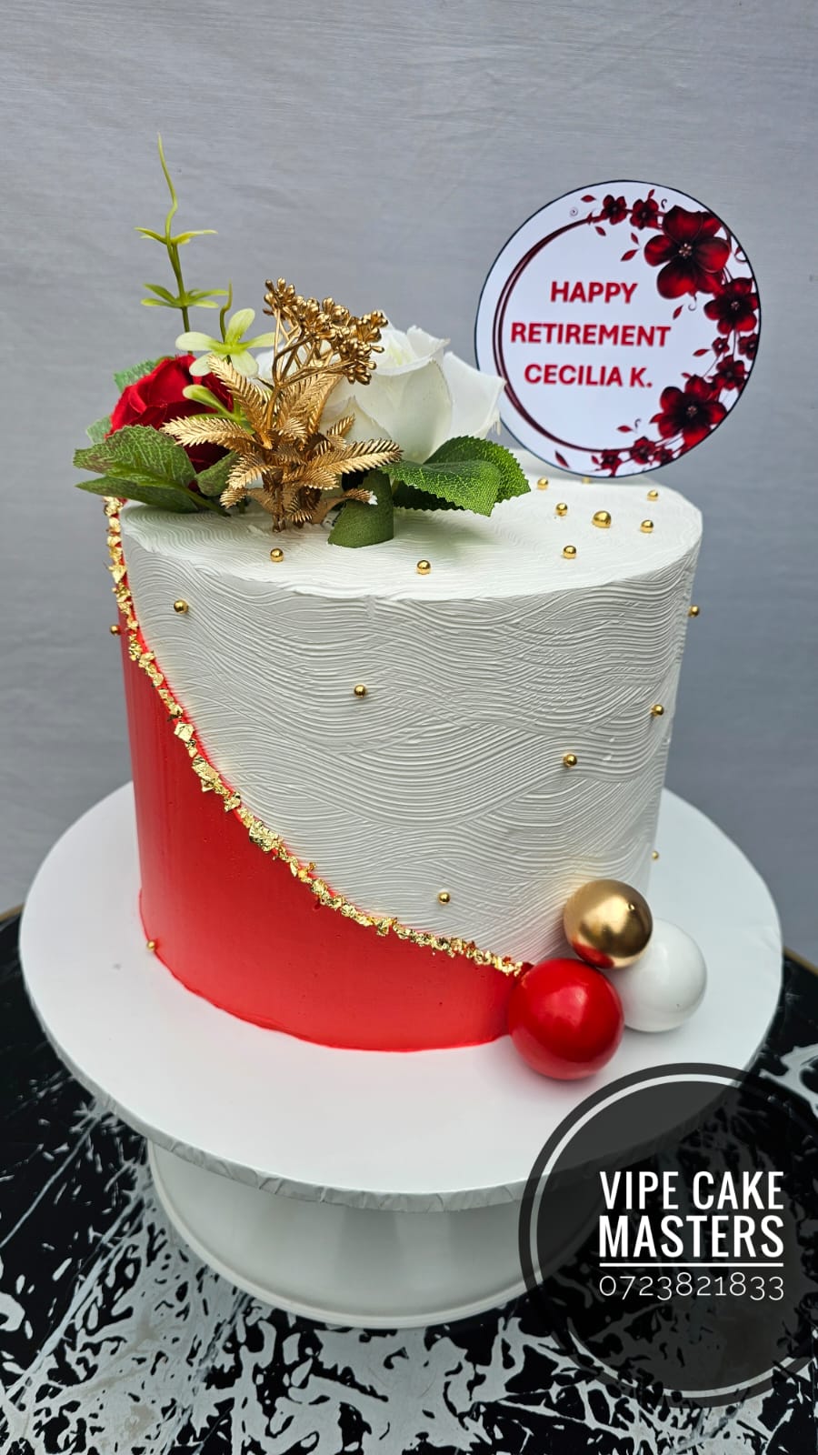 Red and white textured retirement cake with roses, gold foliage and spheres, and Happy Retirement Cecilia K. topper