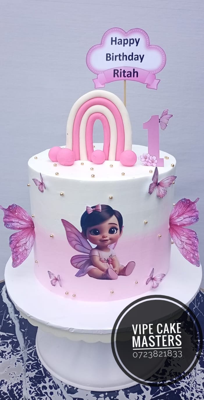 Pink and white first birthday cake for Ritah with a rainbow, butterflies, fairy illustration and number one topper