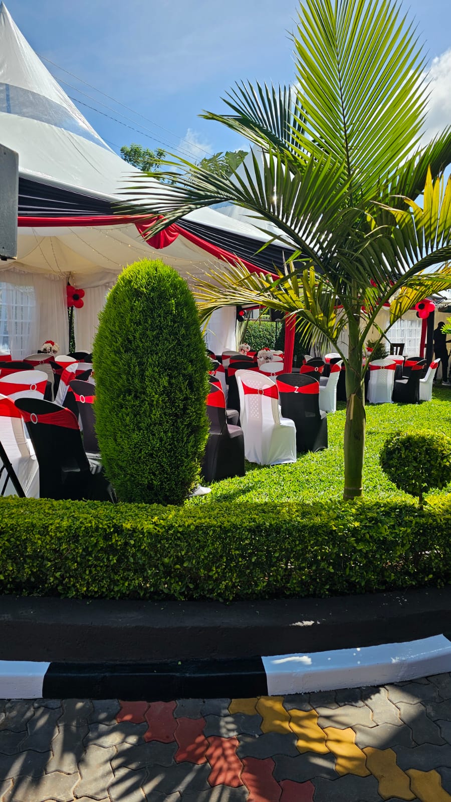 Garden reception marquee with red, black and white decorated chairs and round tables beside green palms