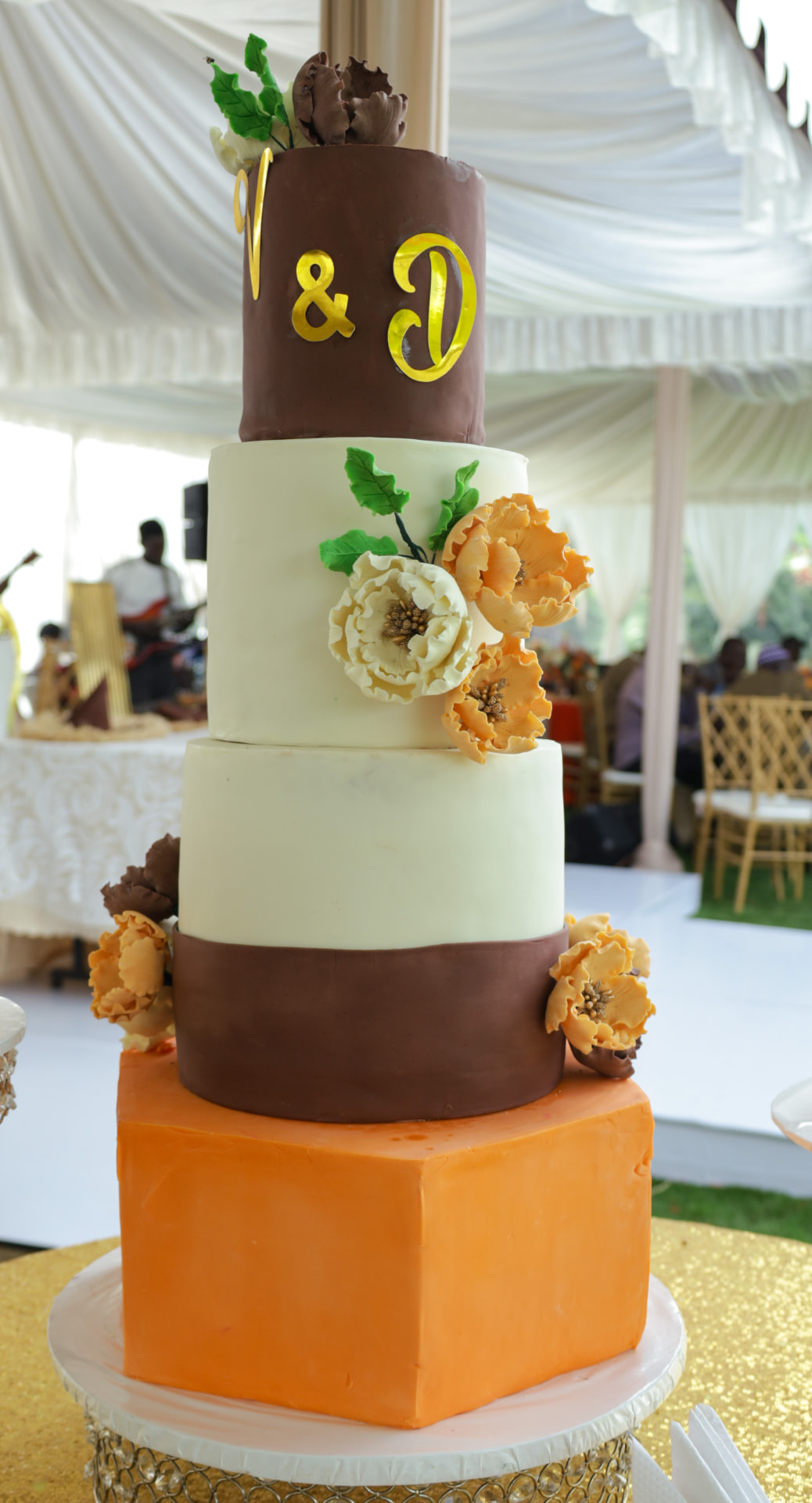 Four-tier chocolate, cream and orange cake with gold lettering and handmade sugar flowers