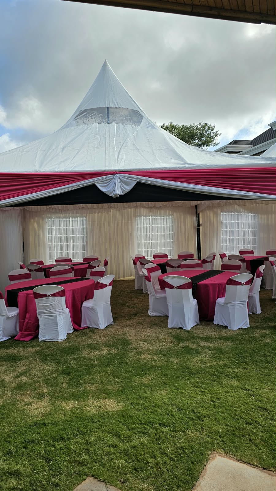 White peaked marquee with pink draping, round reception tables and white covered chairs on a lawn
