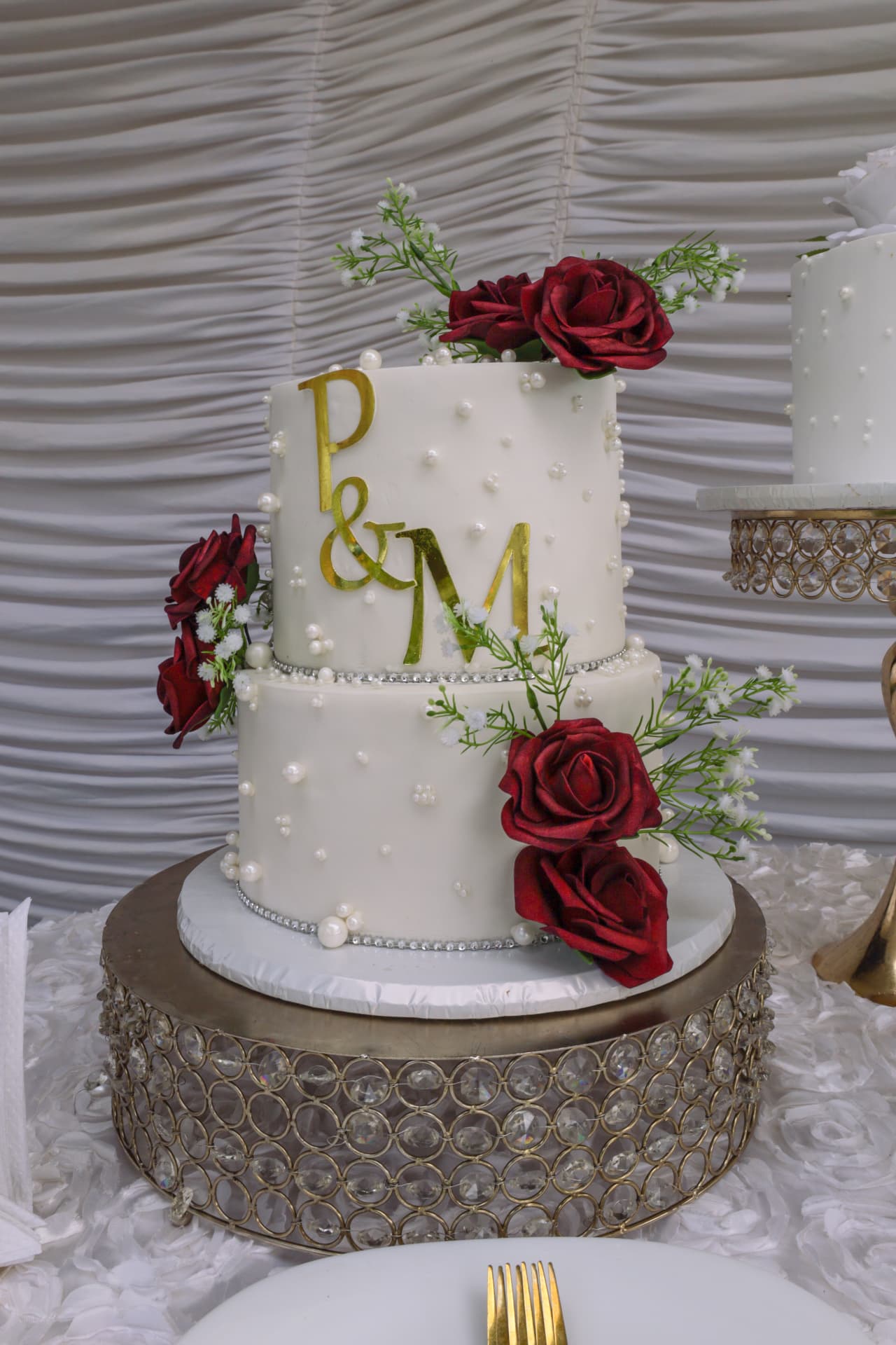 White two-tier cake with gold initials, pearls, crystal band and deep red roses