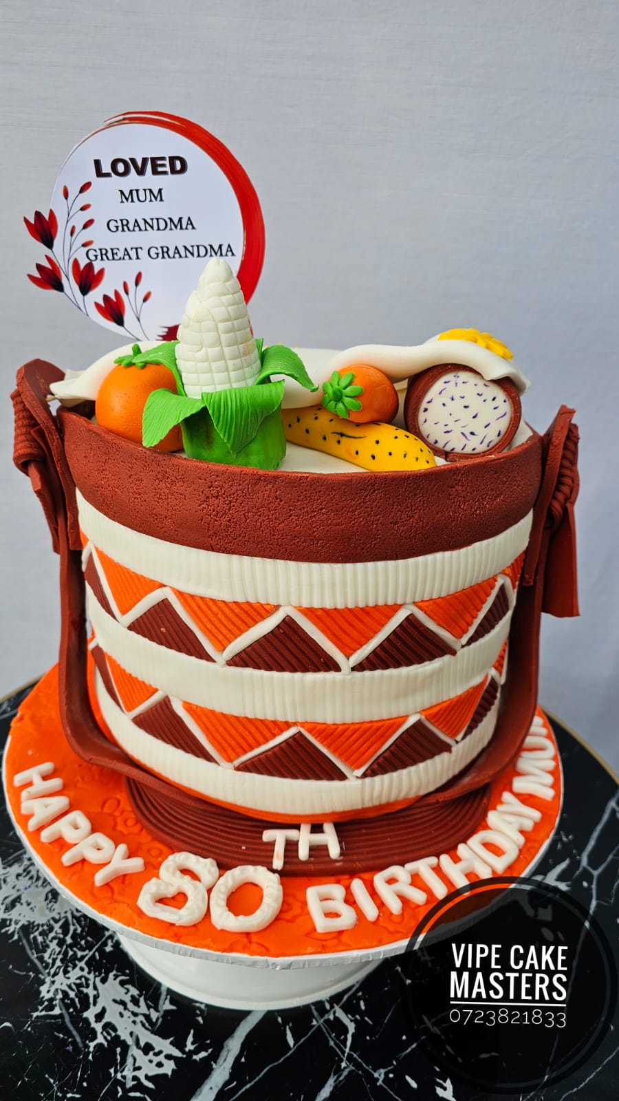 Orange, brown and ivory woven-basket cake for an 80th birthday, topped with handcrafted maize, fruit and a Loved Mum Grandma Great Grandma plaque