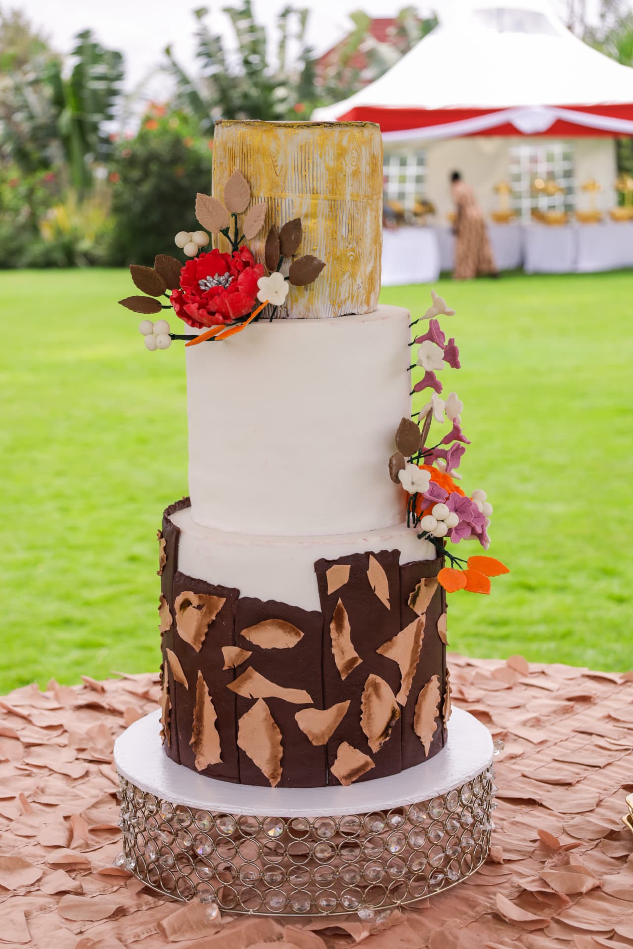 Three-tier cake with chocolate bark panels, gold brushed top tier and autumn sugar flowers on a crystal stand