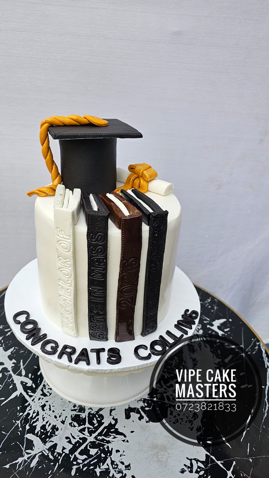 White graduation cake with fondant book spines reading Bachelor of Arts in Mass Communication and a black cap