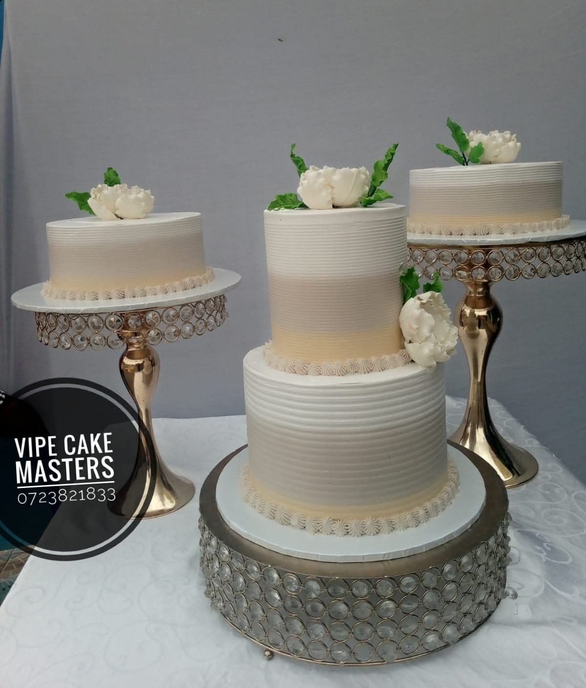 Ivory two-tier wedding cake with two matching side cakes, white sugar peonies and gold crystal stands