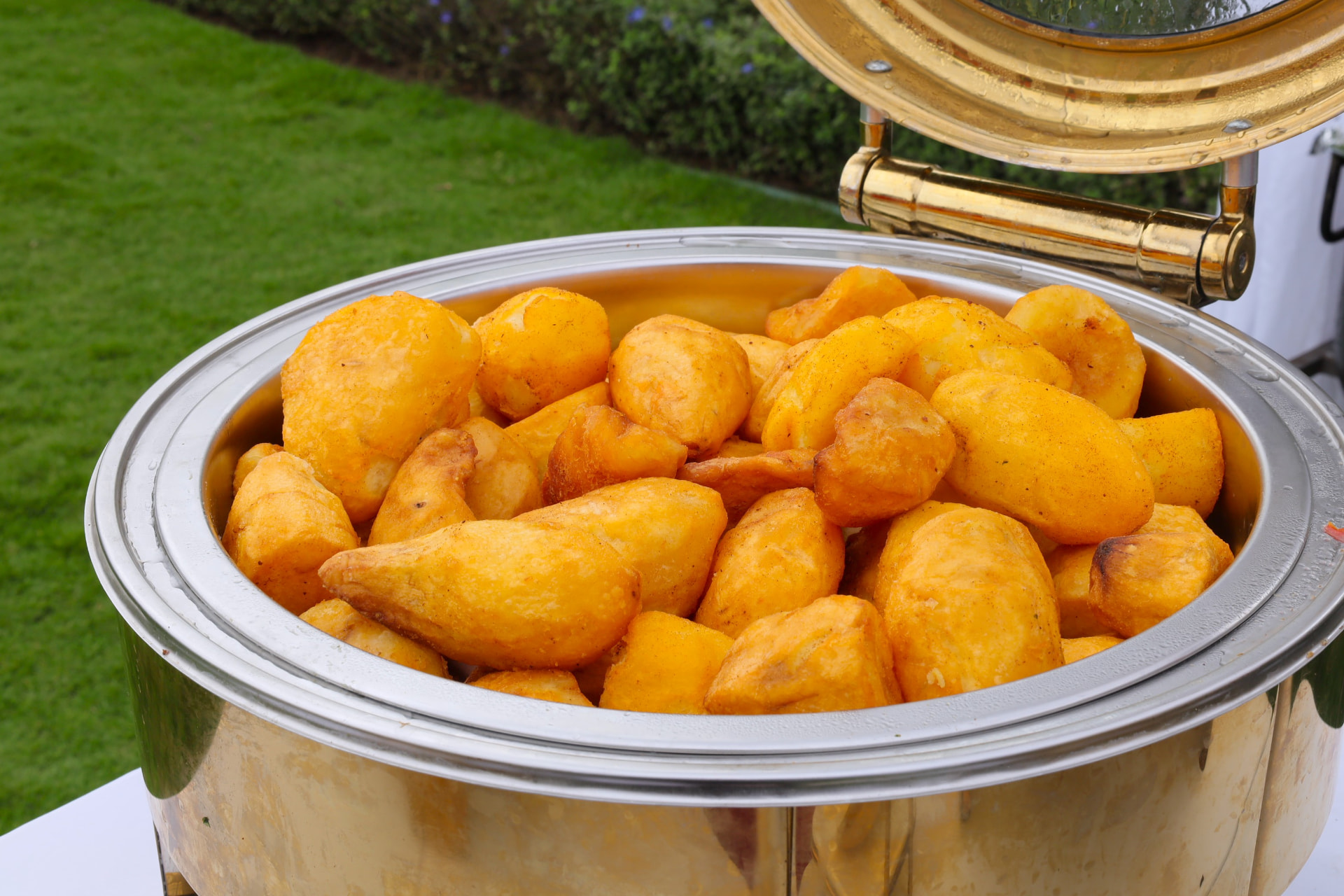 Gold chafer heaped with golden fried potatoes at an outdoor buffet on the lawn