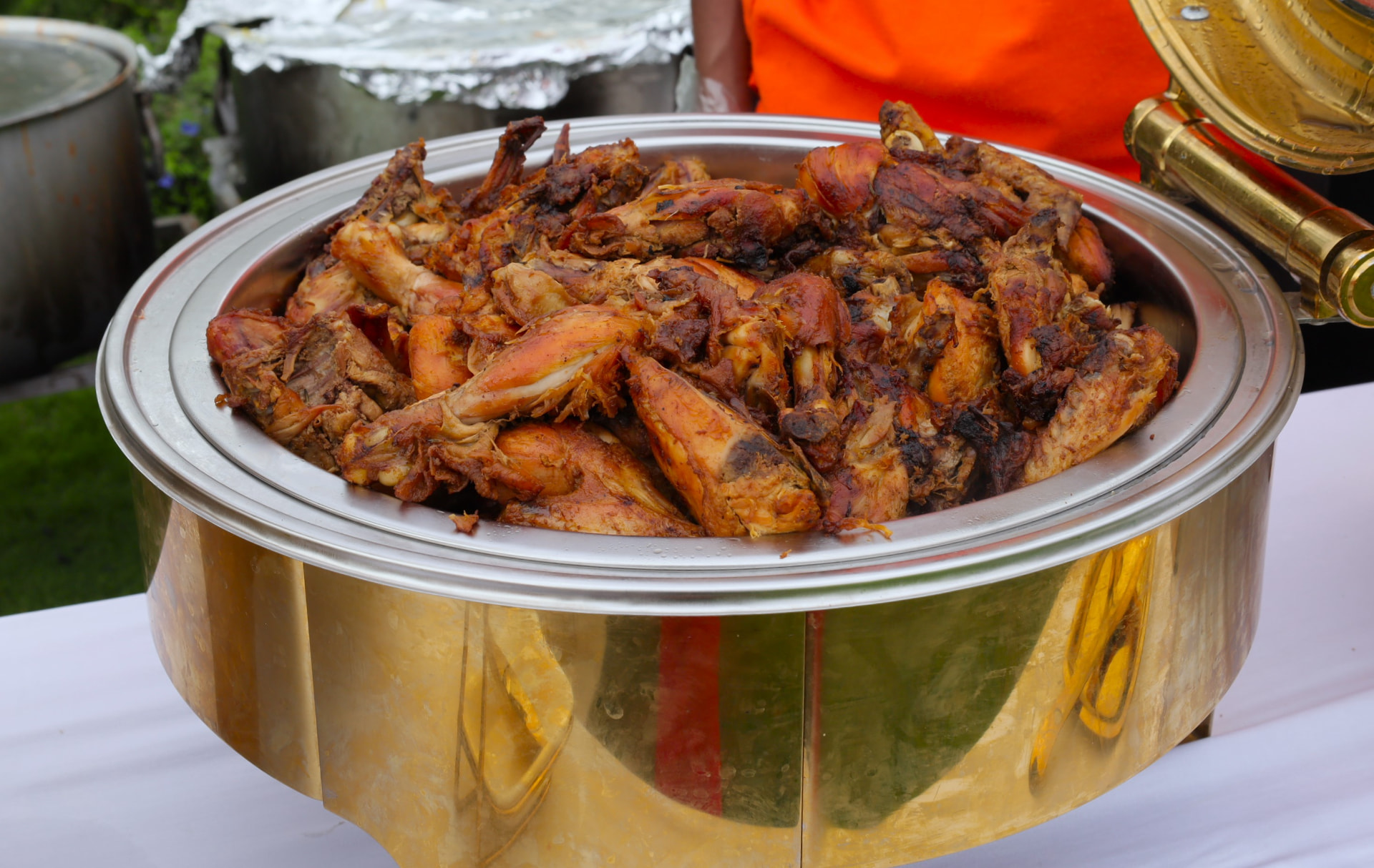 Gold chafer piled with well-roasted seasoned chicken pieces at an outdoor event