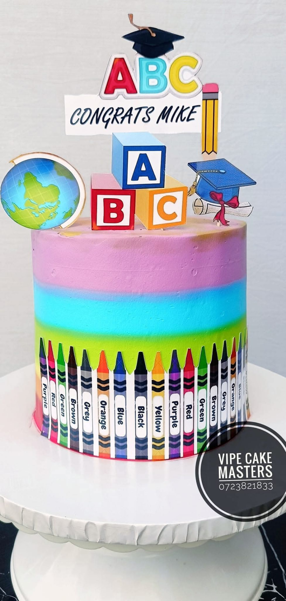 Bright pink, blue and green school graduation cake with crayons, alphabet blocks, globe, diploma and cap