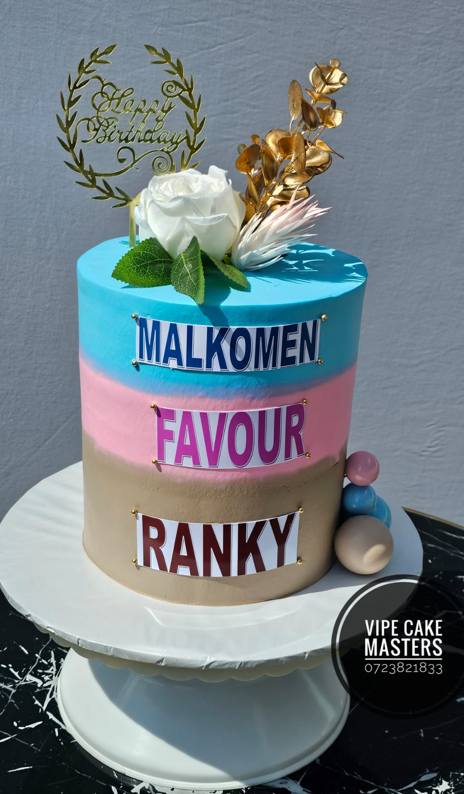 Blue, pink and taupe birthday cake with three name plaques, white rose, gold leaves and Happy Birthday topper