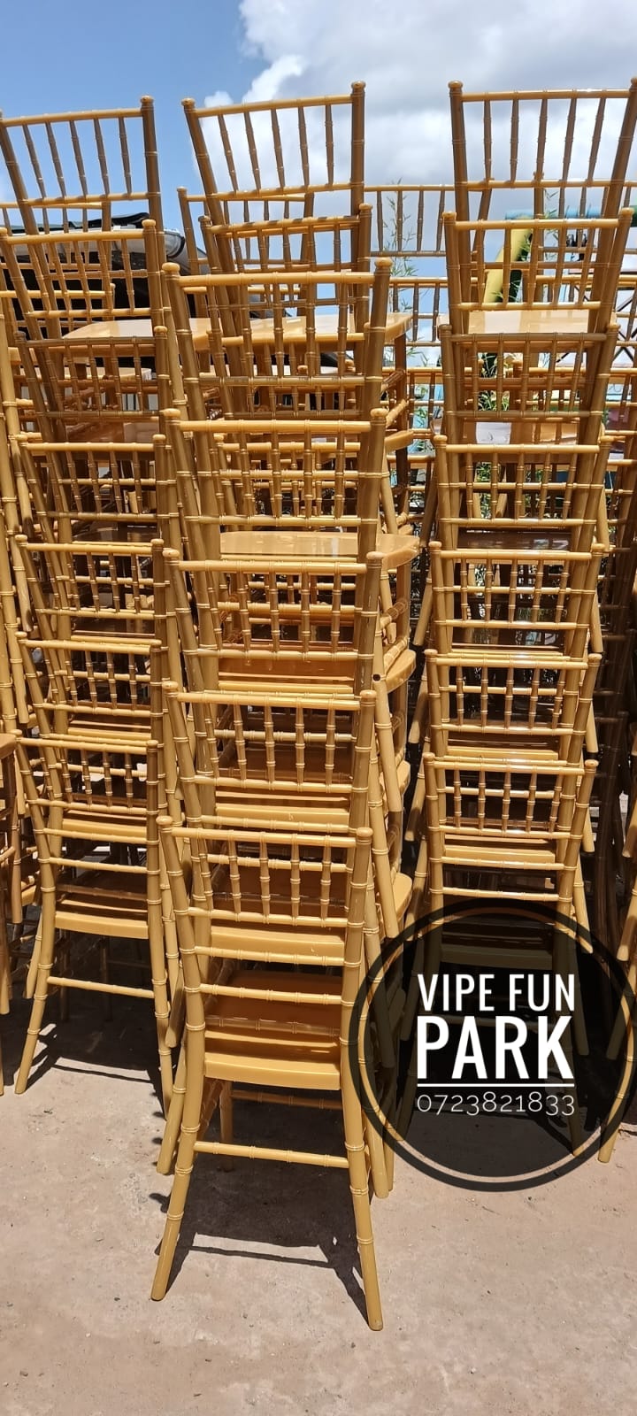 Tall stacks of gold chiavari event chairs stacked outdoors in the yard
