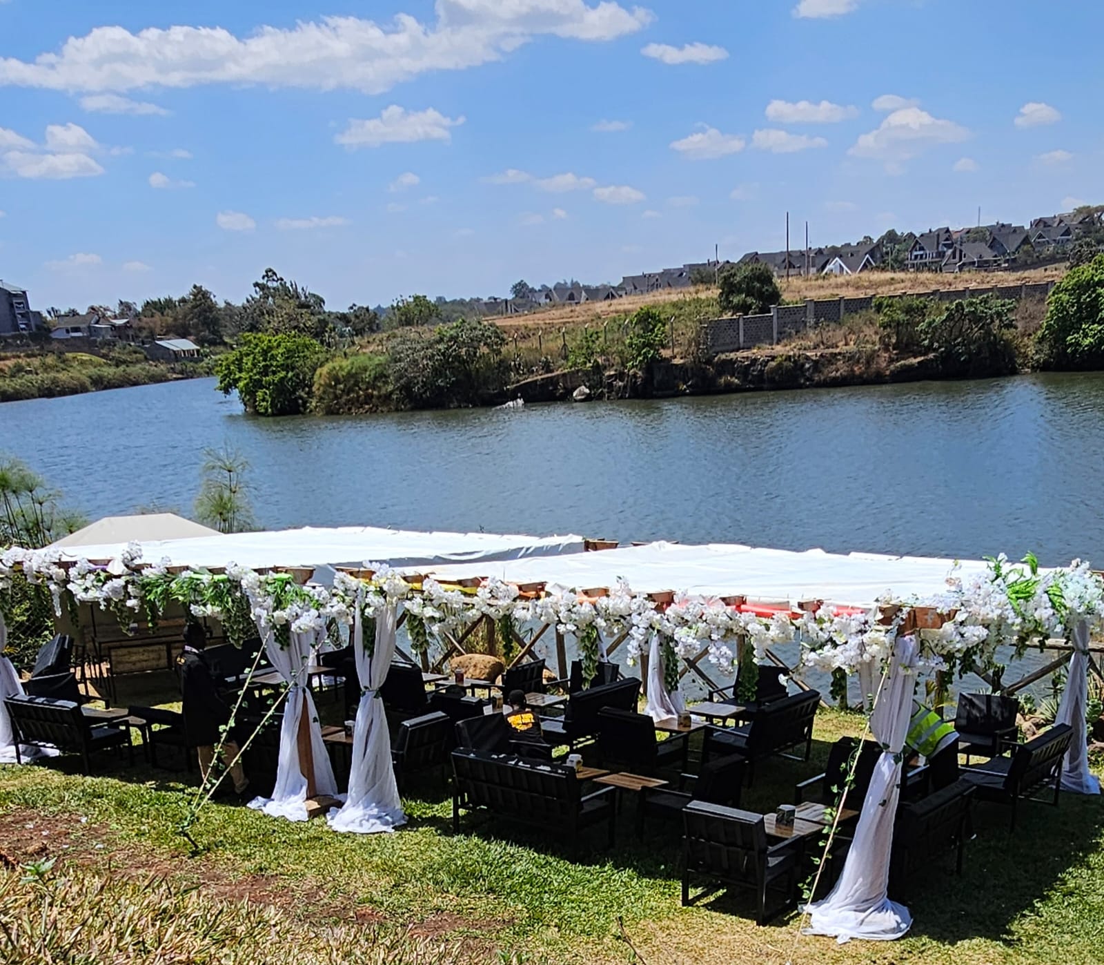 White floral canopies over wooden lounge seating on a lawn beside the lake