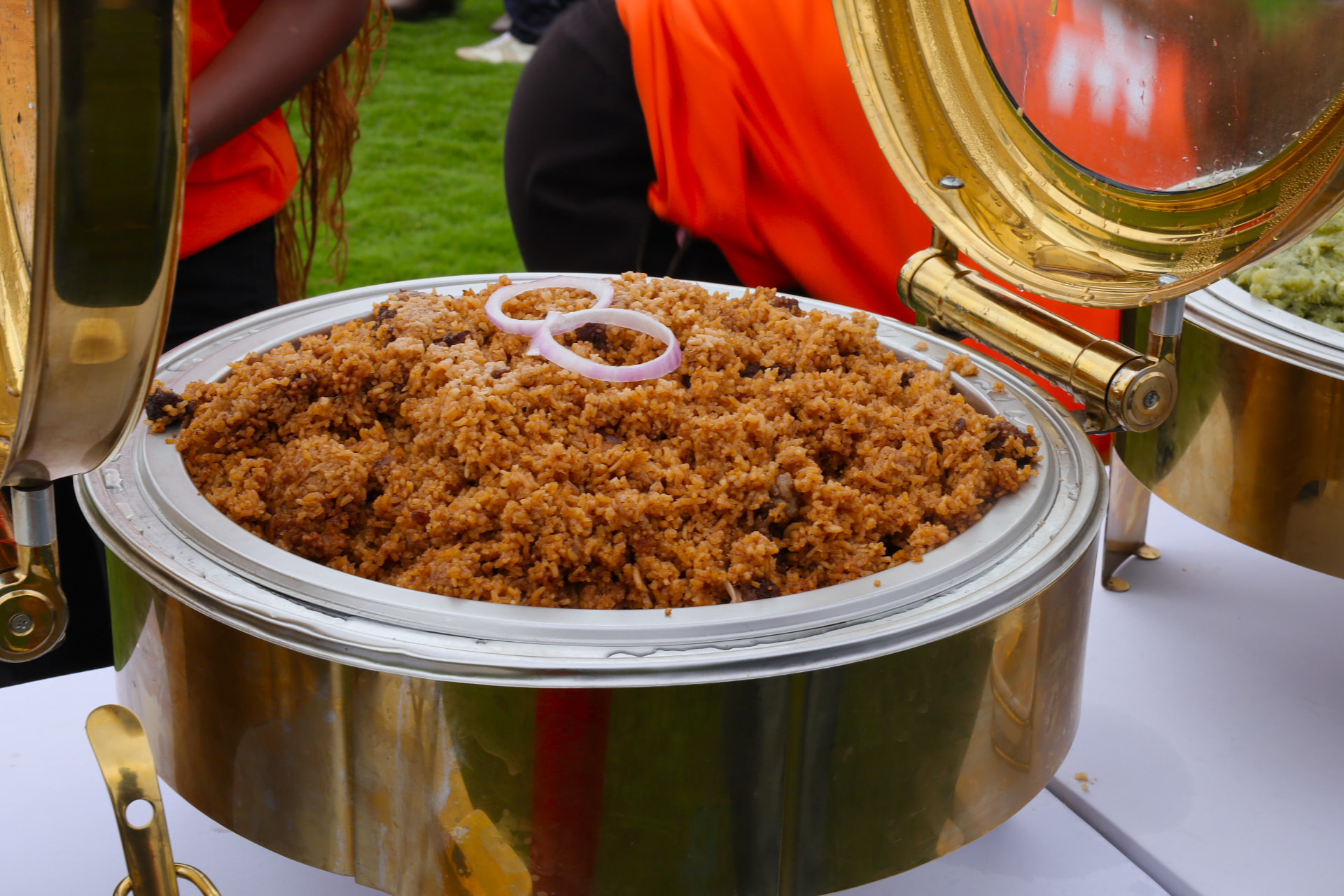 Large gold chafer filled with spiced pilau rice garnished with onion rings at an outdoor event