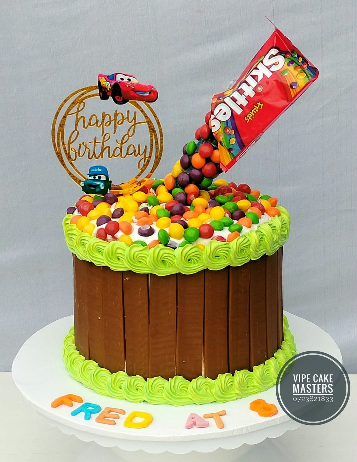 Chocolate-finger birthday cake with green piping and a pouring Skittles packet topper for Fred at 8