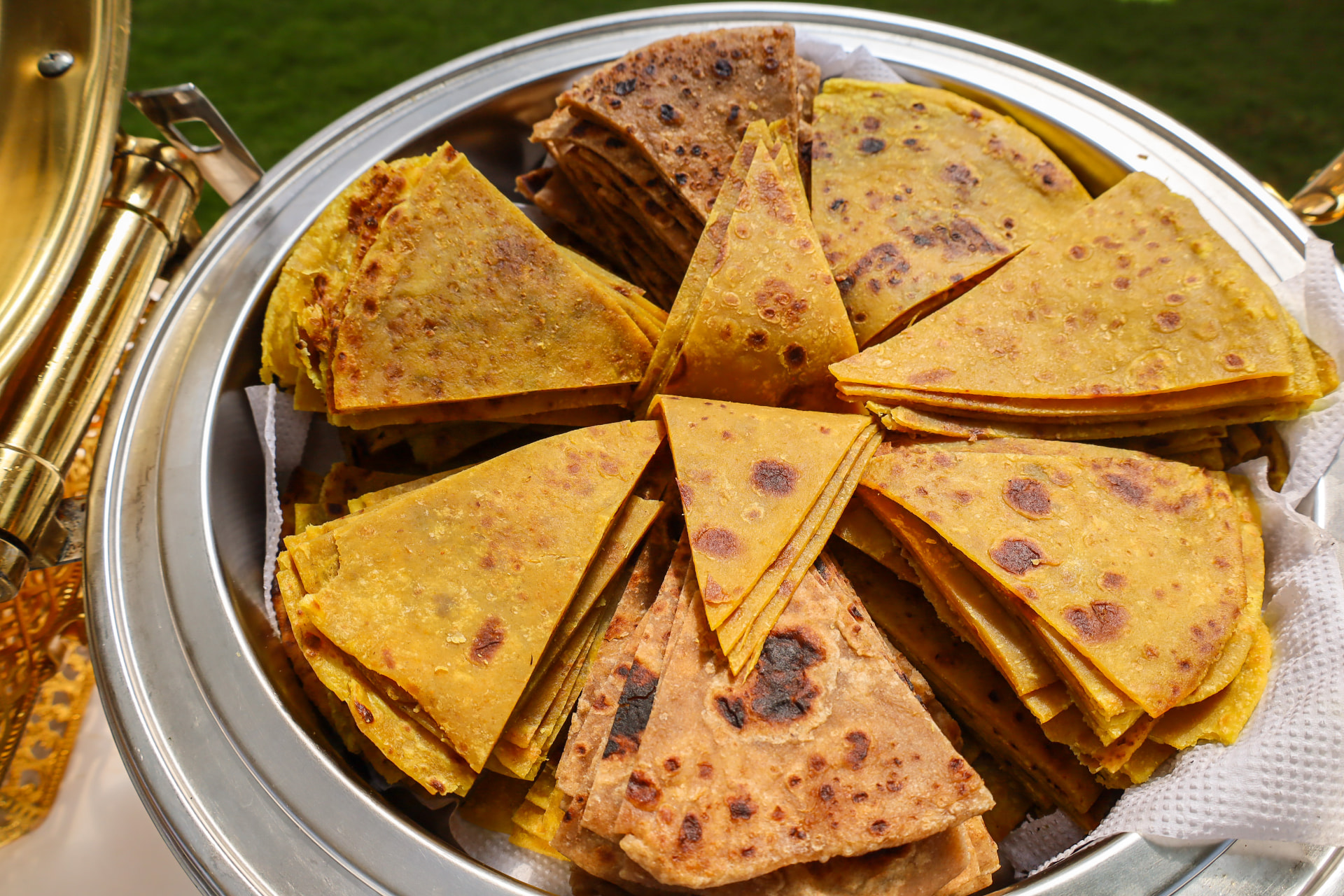 Chafer stacked with golden chapatis folded into triangles at an outdoor buffet