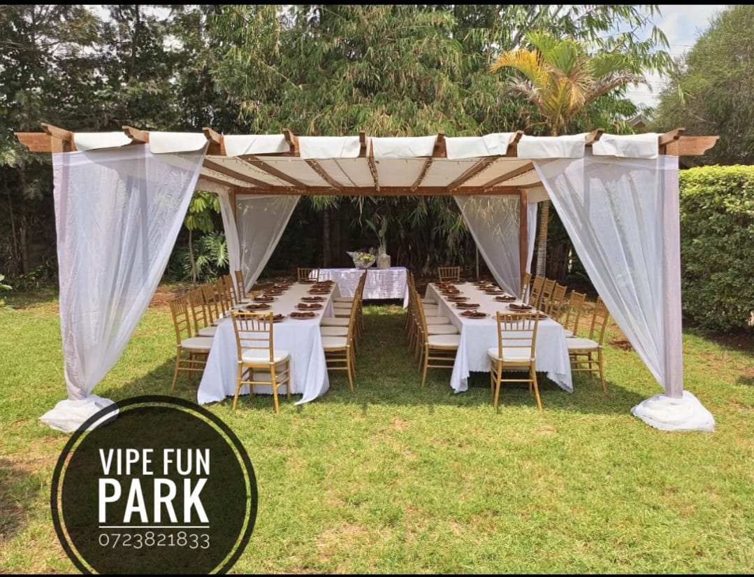 Wooden pergola with white draping over long tables and gold chiavari chairs on the lawn