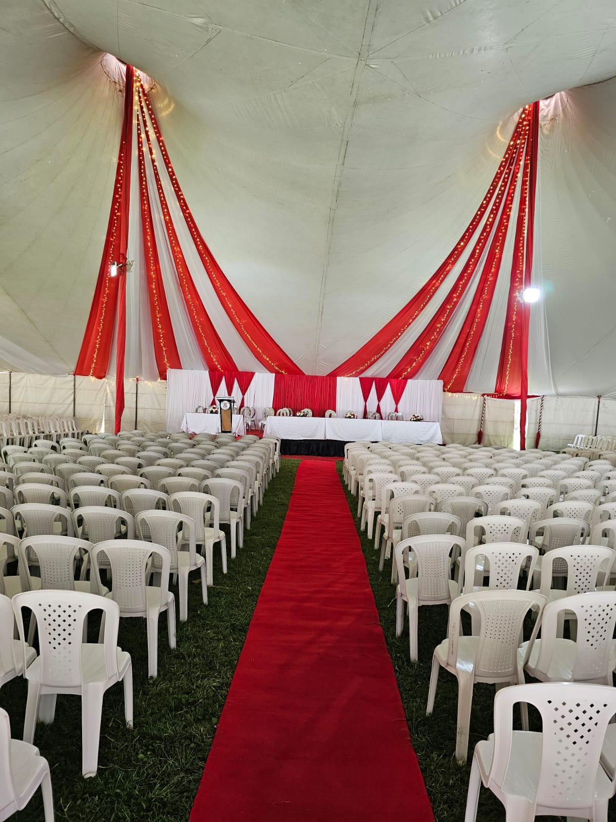 Red carpet aisle between rows of white chairs beneath a marquee with red and white draping