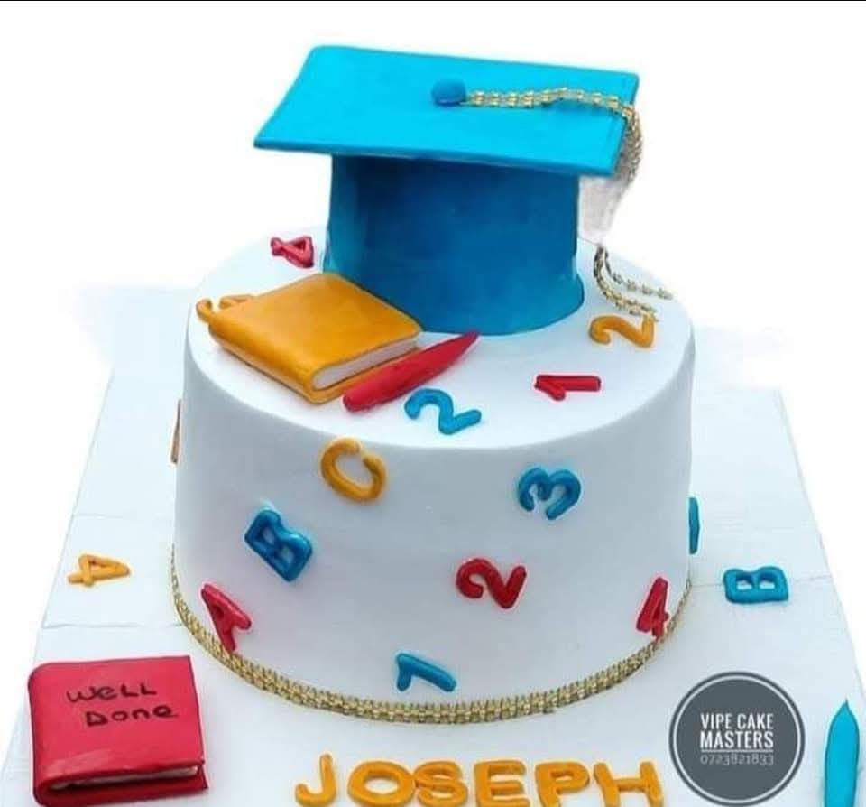 White graduation cake with blue cap, colourful letters and numbers, books and a personalised Joseph name