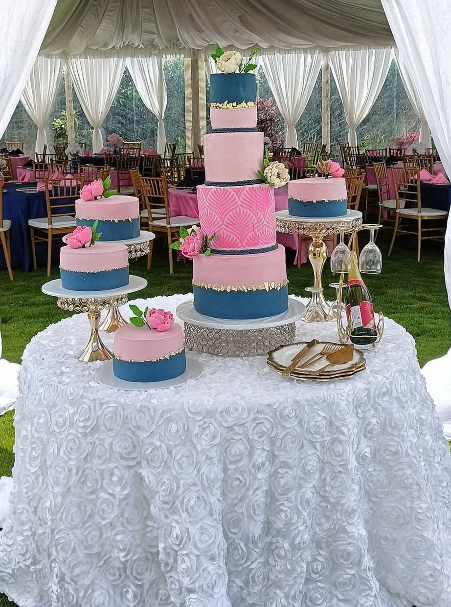 Pink and navy tiered celebration cake with matching single-tier cakes, pink peonies and gold leaf detailing on a white rosette table under a marquee