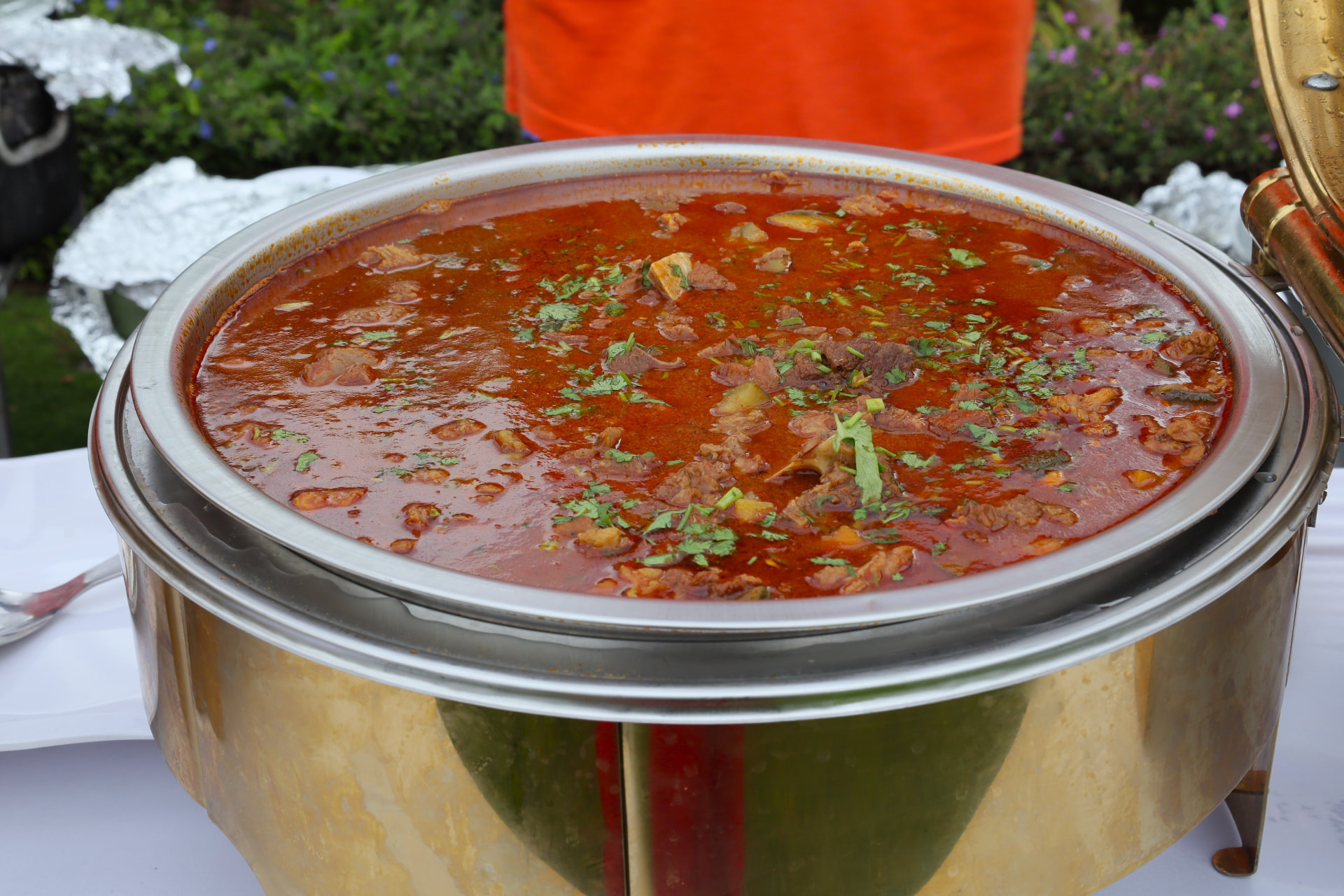 Large gold chafer of rich tomato beef stew garnished with coriander served outdoors