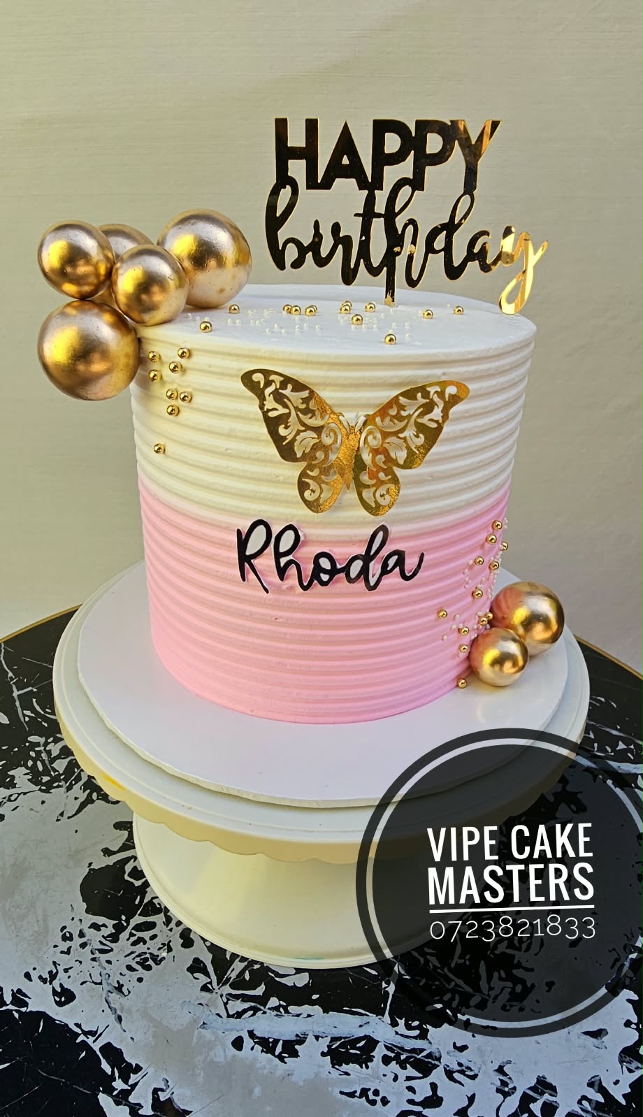 Pink and white ribbed birthday cake with gold butterfly, gold spheres, Rhoda lettering and Happy Birthday topper