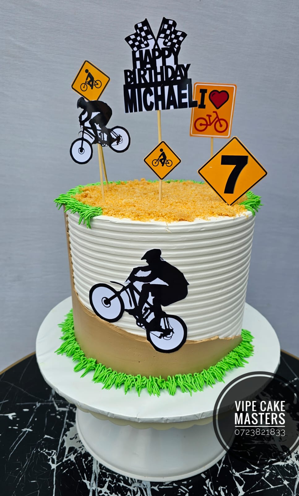 White and gold cycling themed seventh birthday cake with bike silhouettes, road signs and Happy Birthday Michael topper