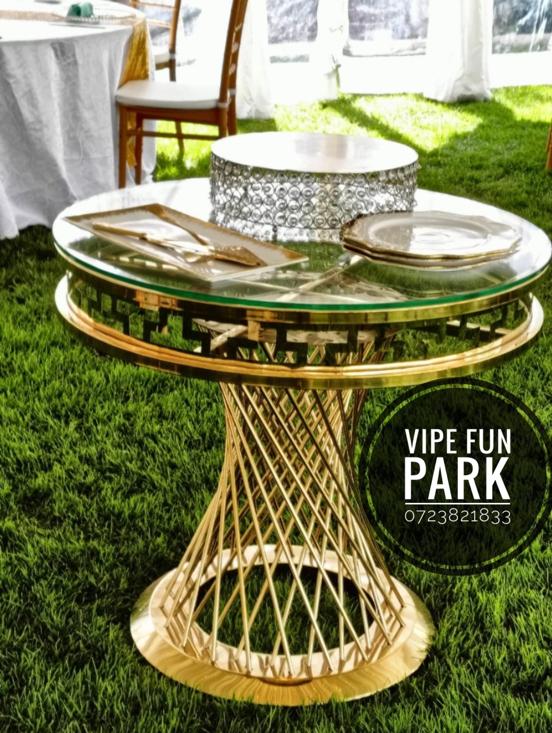 Round glass-top gold table with a crystal cake stand, gold cutlery set and serving plates