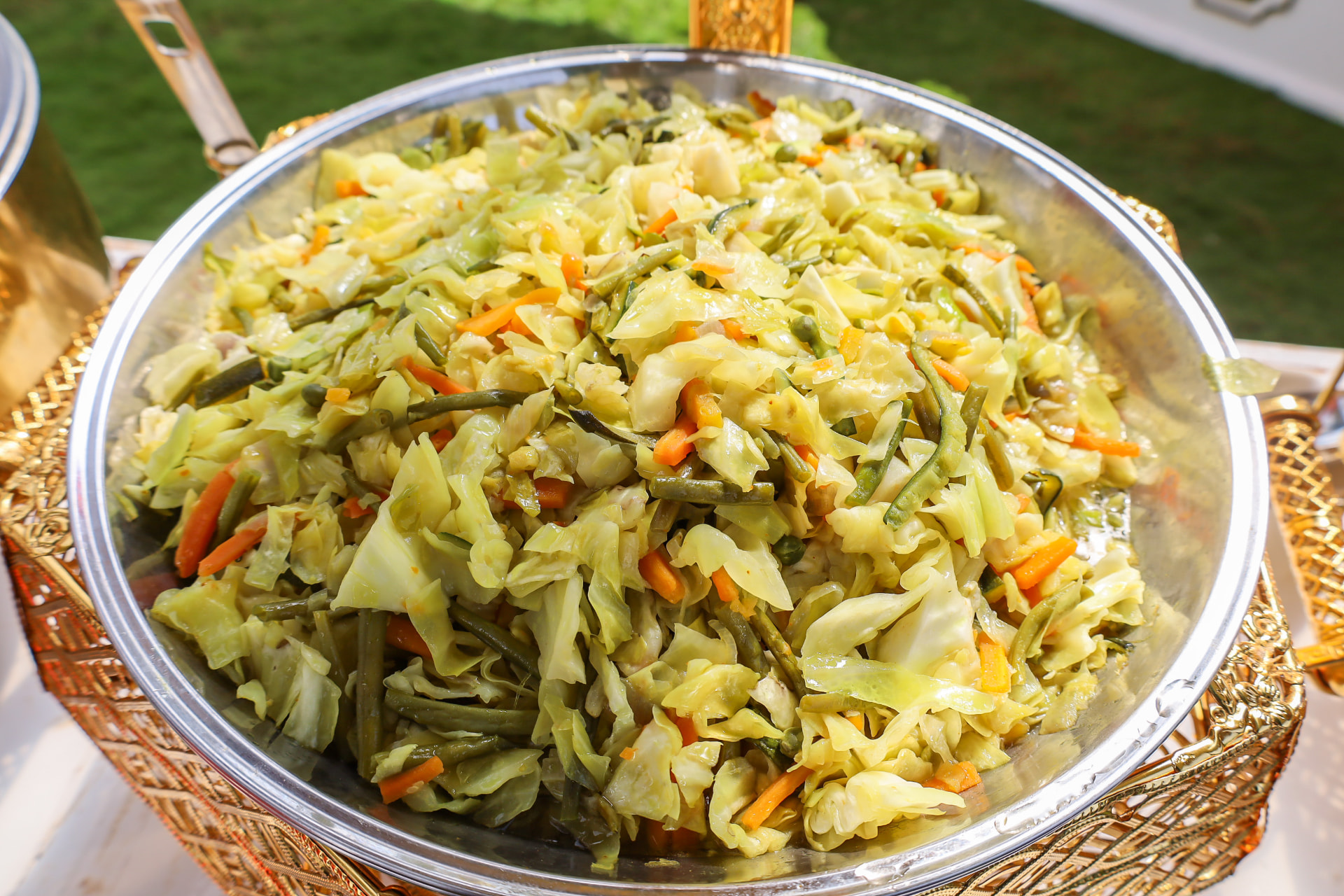 Gold tray of fresh cabbage, carrot and green bean salad at an outdoor event