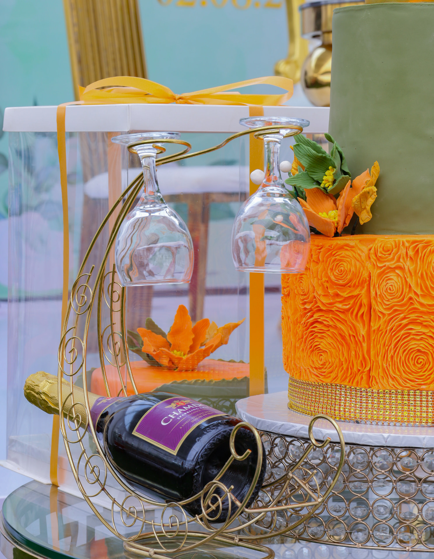 Gold bottle holder, glassware and colourful tiered cake arranged for an event