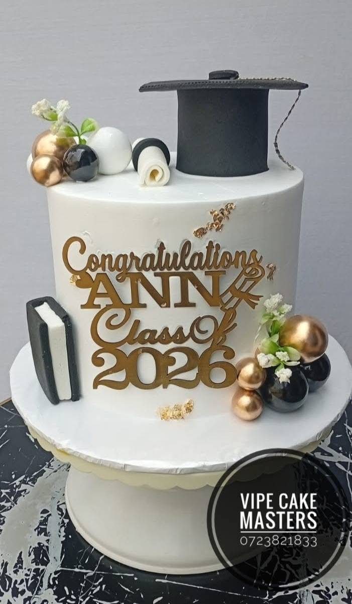 White graduation cake with black cap, gold Congratulations Ann Class of 2026 topper and rose gold spheres