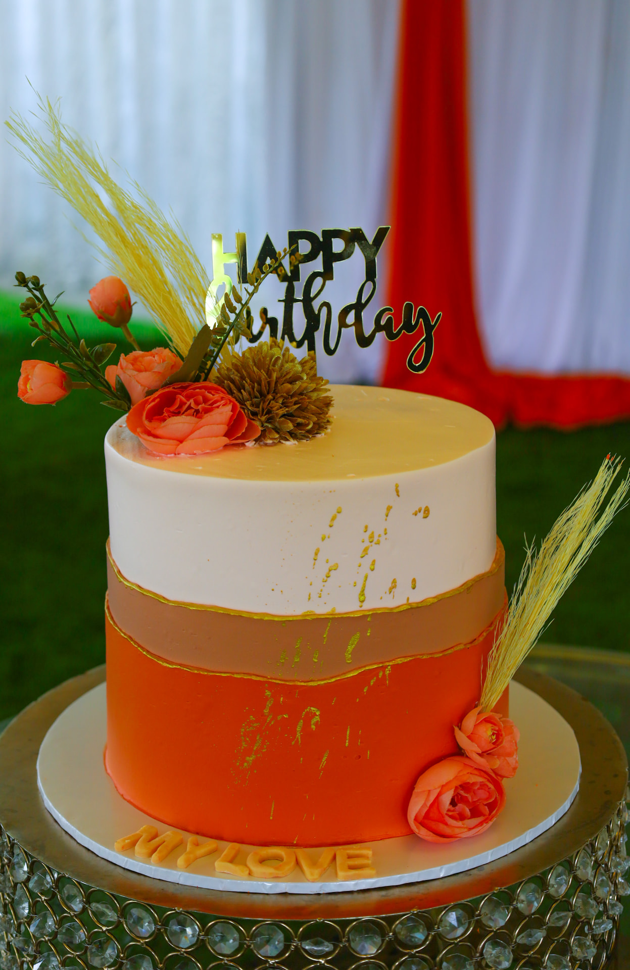 Orange and cream birthday cake with gold Happy Birthday topper, wheat stalks and orange roses