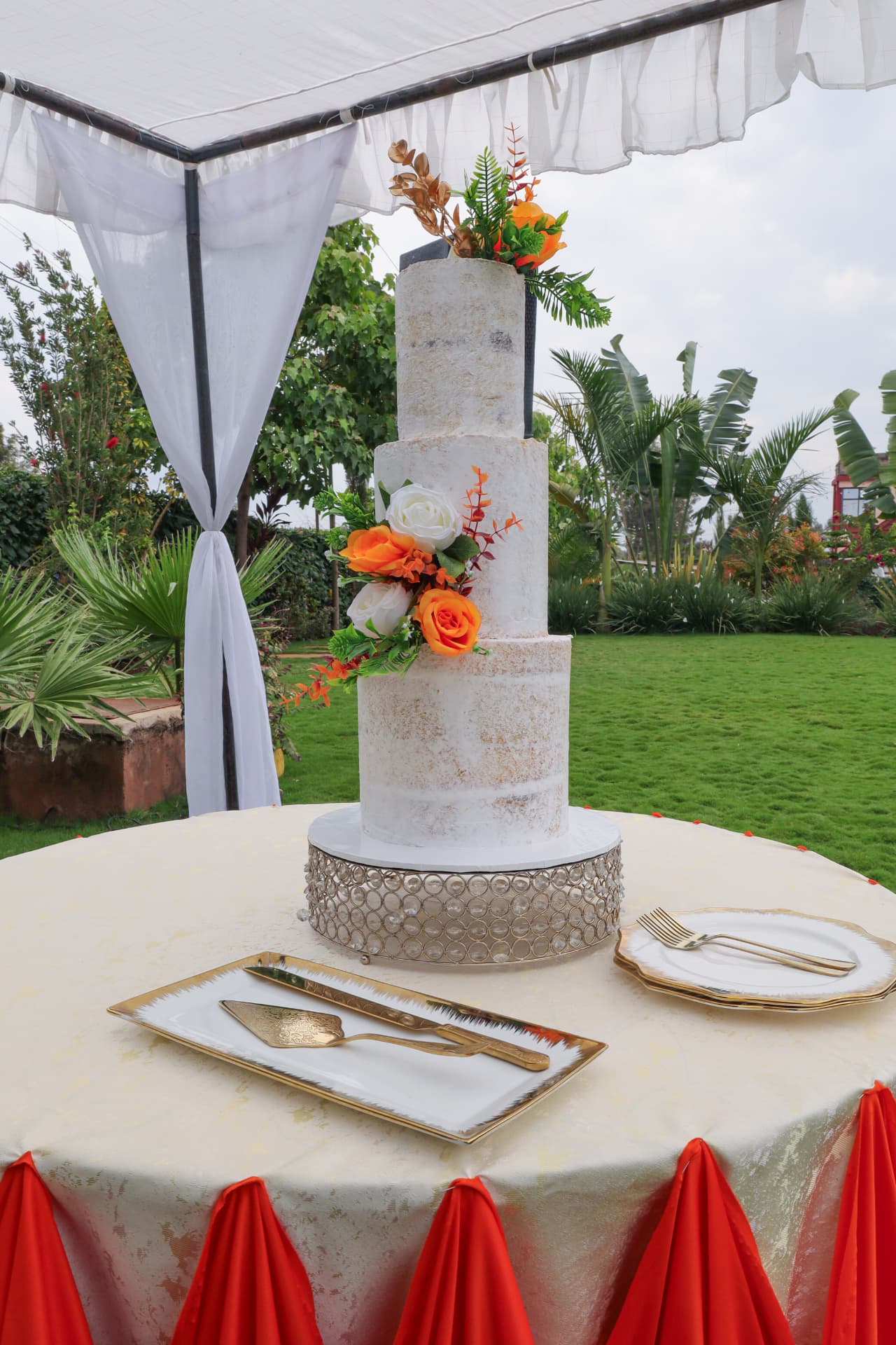 Tall marbled three-tier wedding cake with fresh orange and white roses under a white canopy