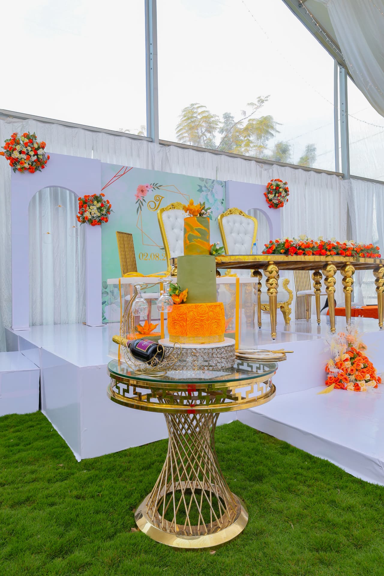 Styled outdoor event stage and cake display with white seating and floral decor
