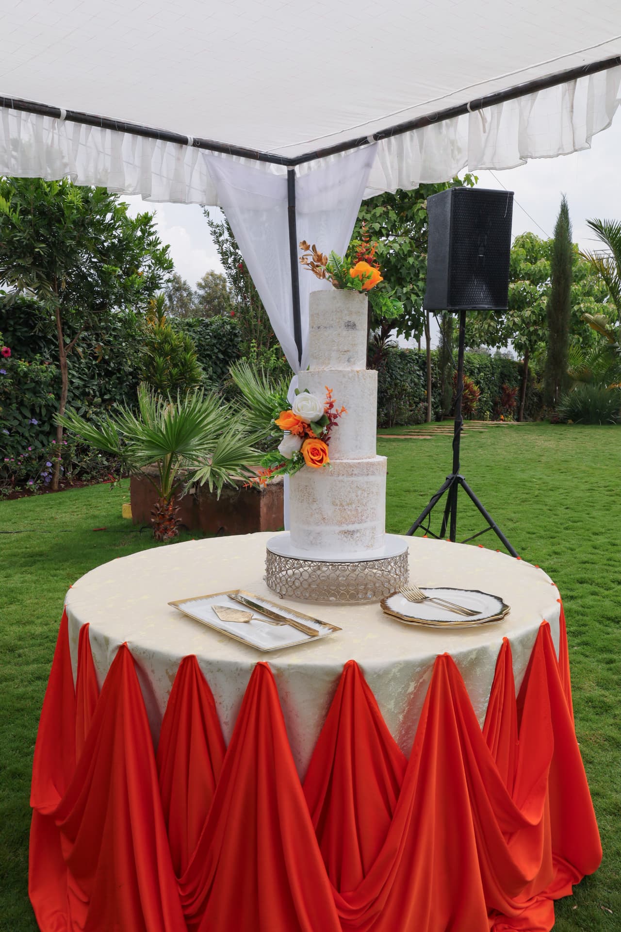 Marbled wedding cake on a gold-trimmed table with red draping in a lush garden setting