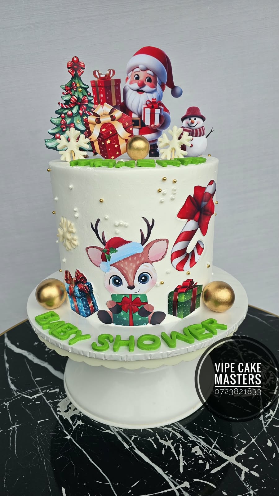 White baby shower cake with Christmas reindeer, Santa, tree, gifts, candy cane and green Baby Shower lettering