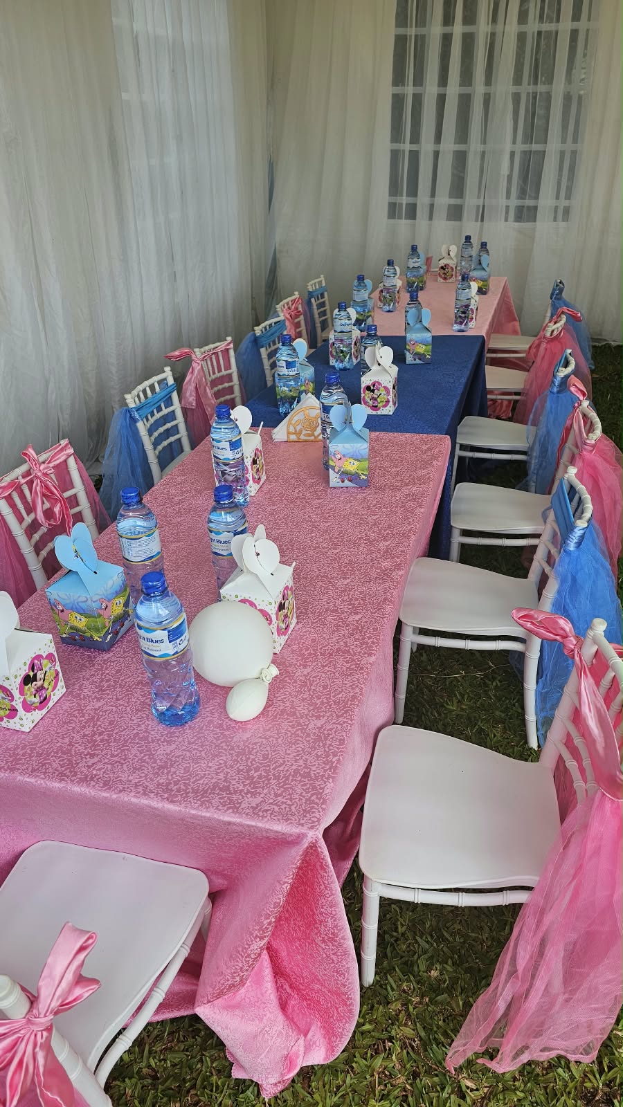 Children’s party tables with pink and blue linens, white chairs, matching bows and character favour boxes